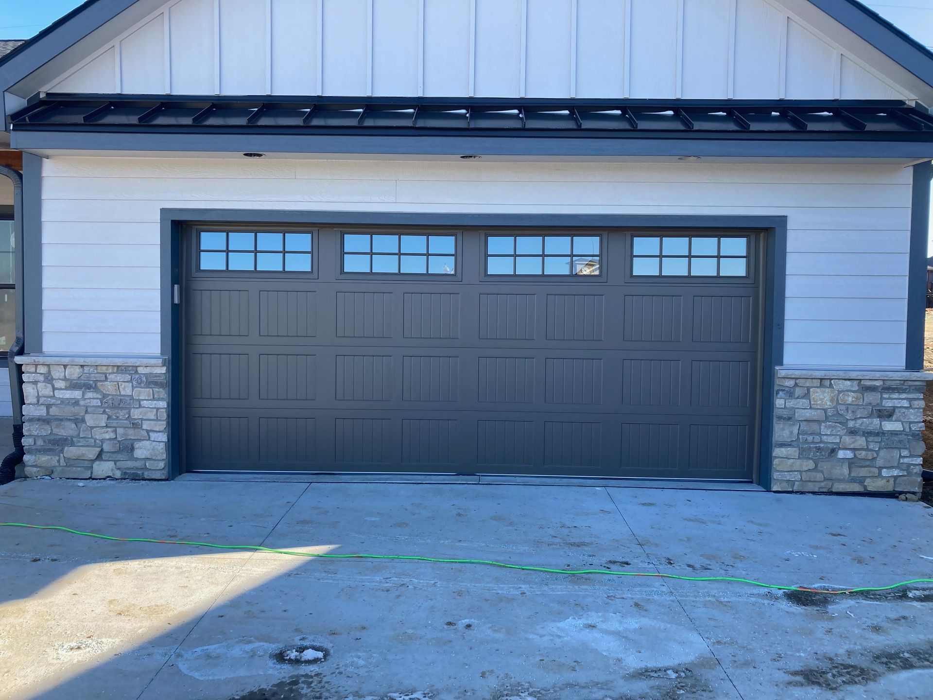 Front view of a house with a dark gray garage door and stone accents under a gabled roof