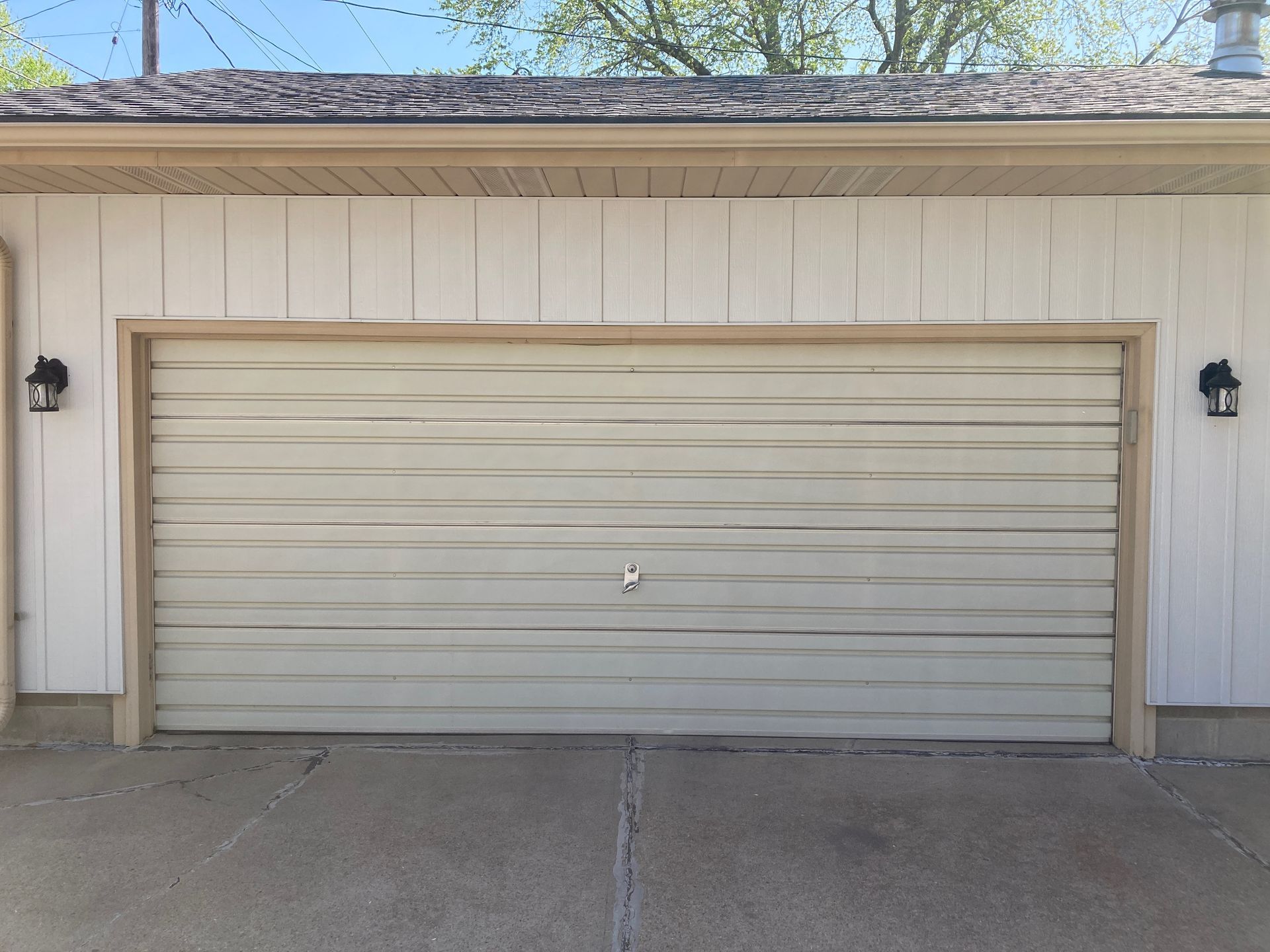 Beige two-car garage door on a white house with concrete driveway in front
