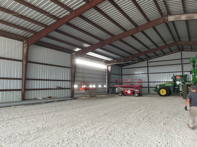 Large metal barn interior with tractors, a red trailer, and gravel floor; one person stands at right.