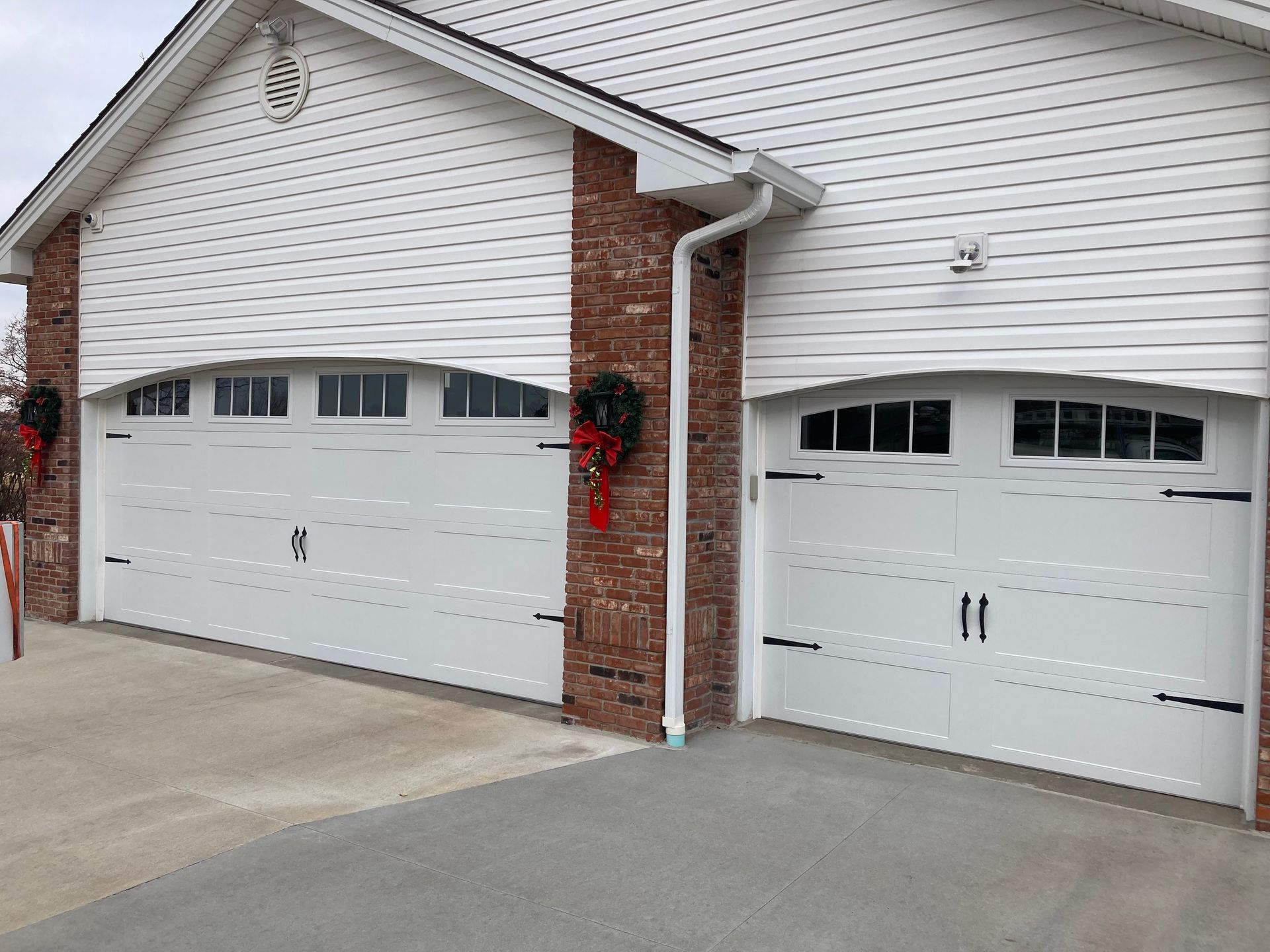 Two white garage doors with arched windows on a brick-and-siding house exterior