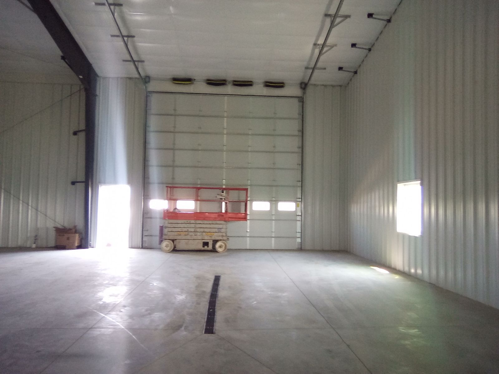 Empty industrial warehouse interior with a closed loading door and a small lift or forklift near the back wall