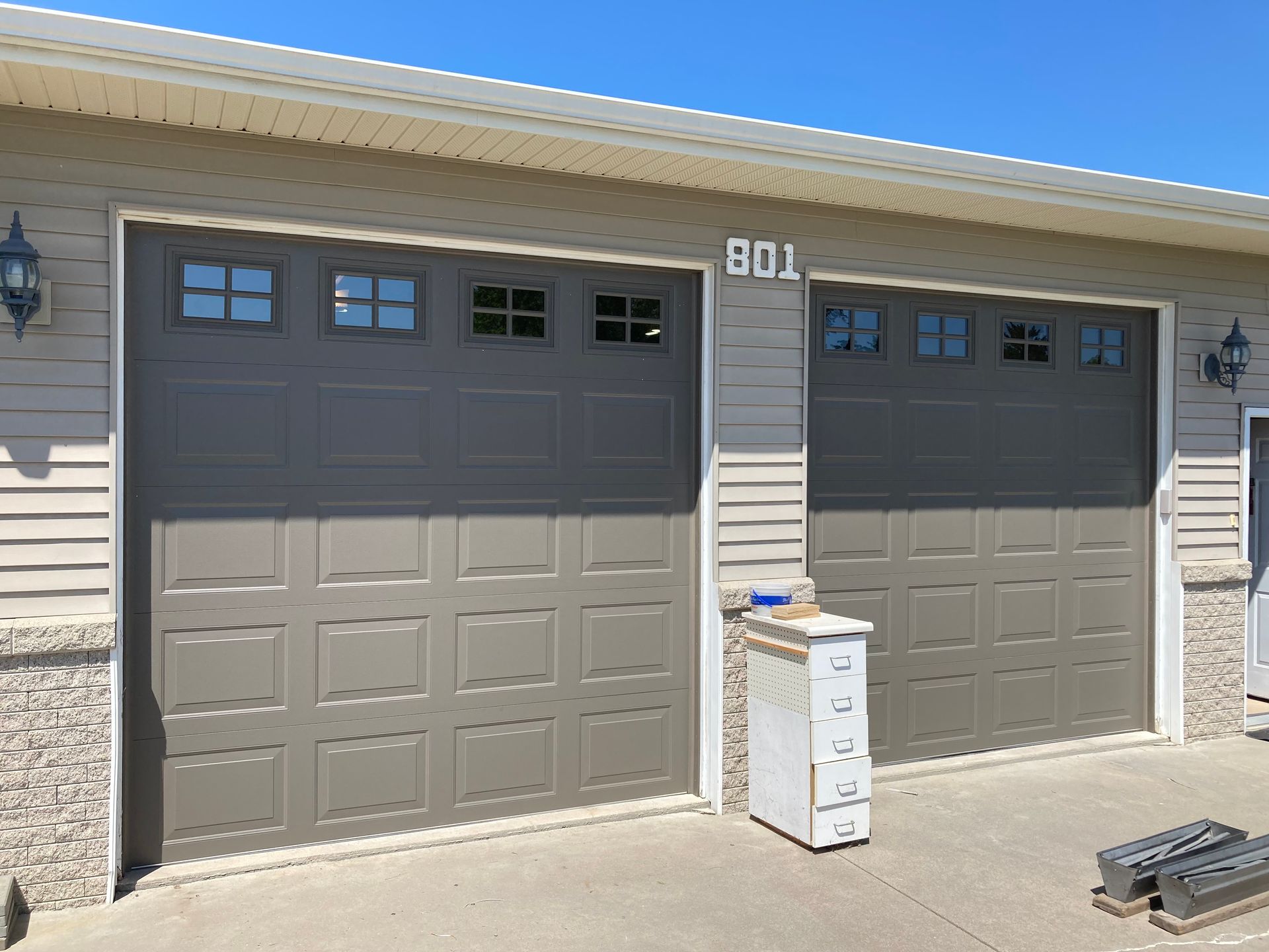 Two-panel garage with gray doors and house number 901 on a beige home exterior under a blue sky