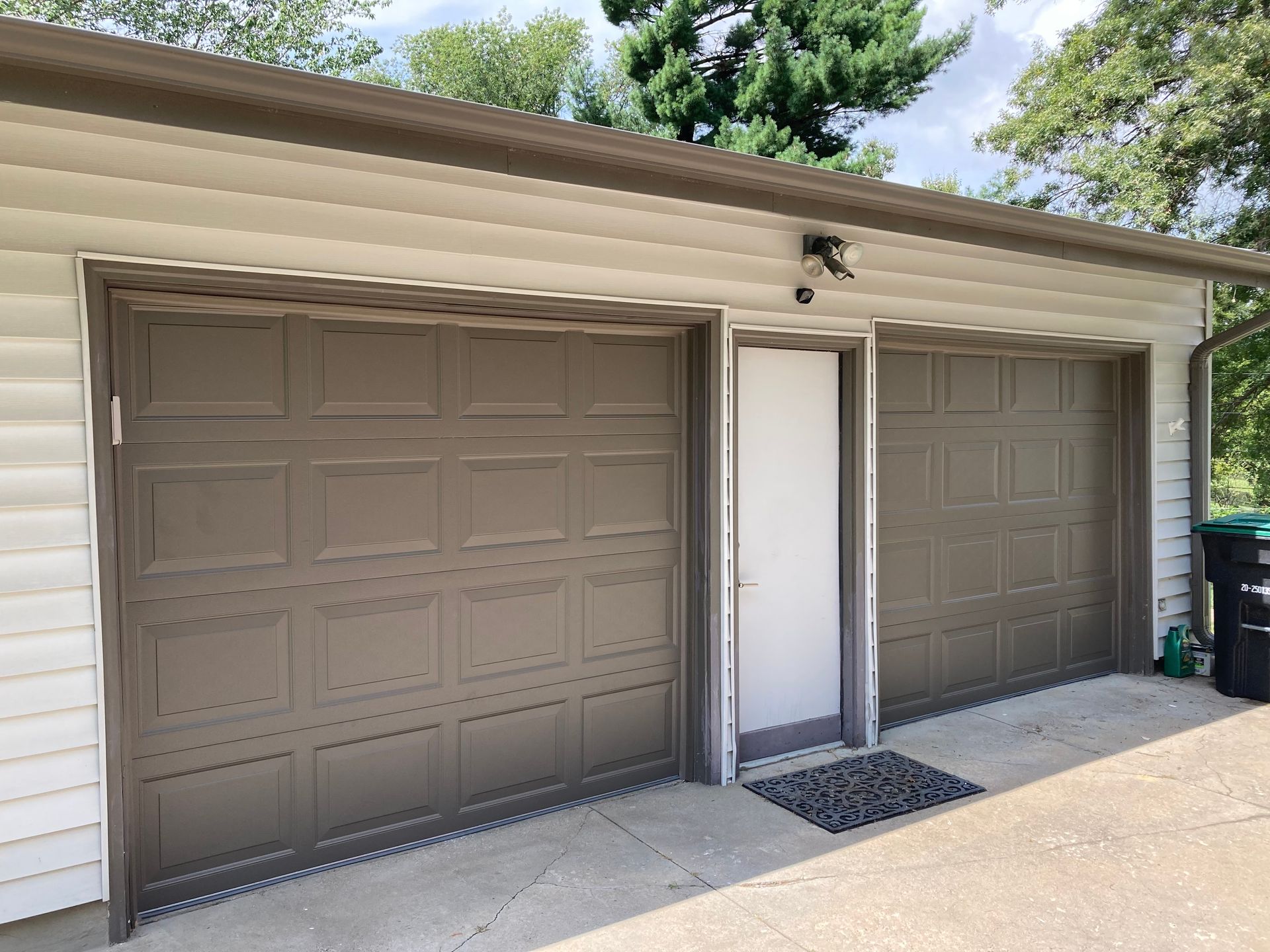 Two brown garage doors beside a white side entry on a house exterior