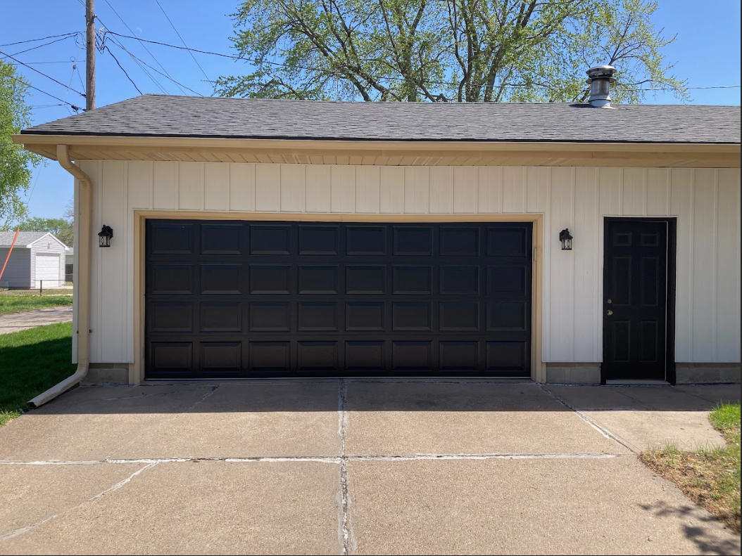 Single-story beige garage with a black door and side entry door, viewed from the driveway.