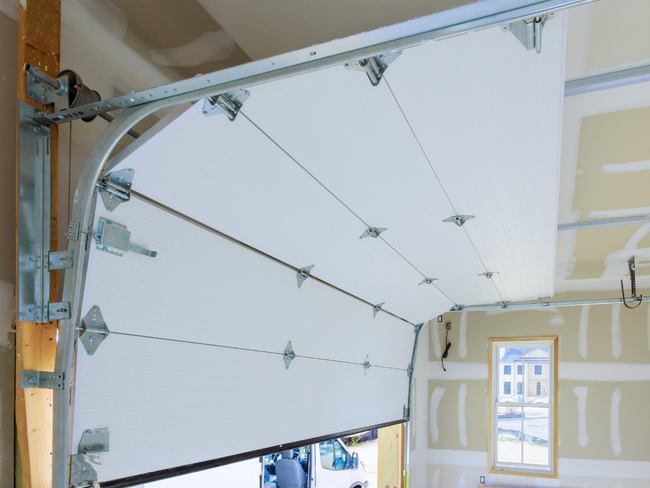 Garage door, partially open, inside a garage with exposed framing and drywall.