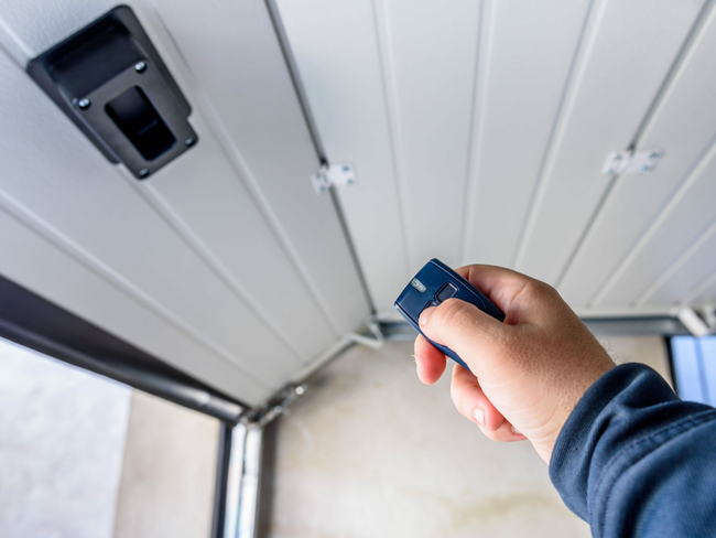 Hand pressing a remote control to open a white garage door.