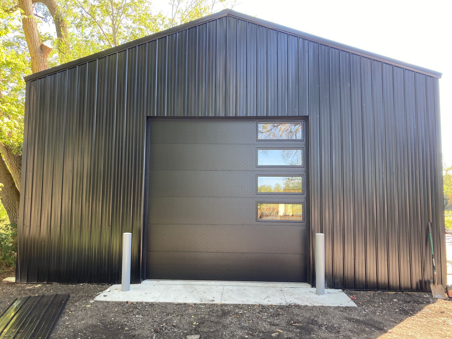 Black corrugated metal building with a large garage-style door and small windows on the right side.