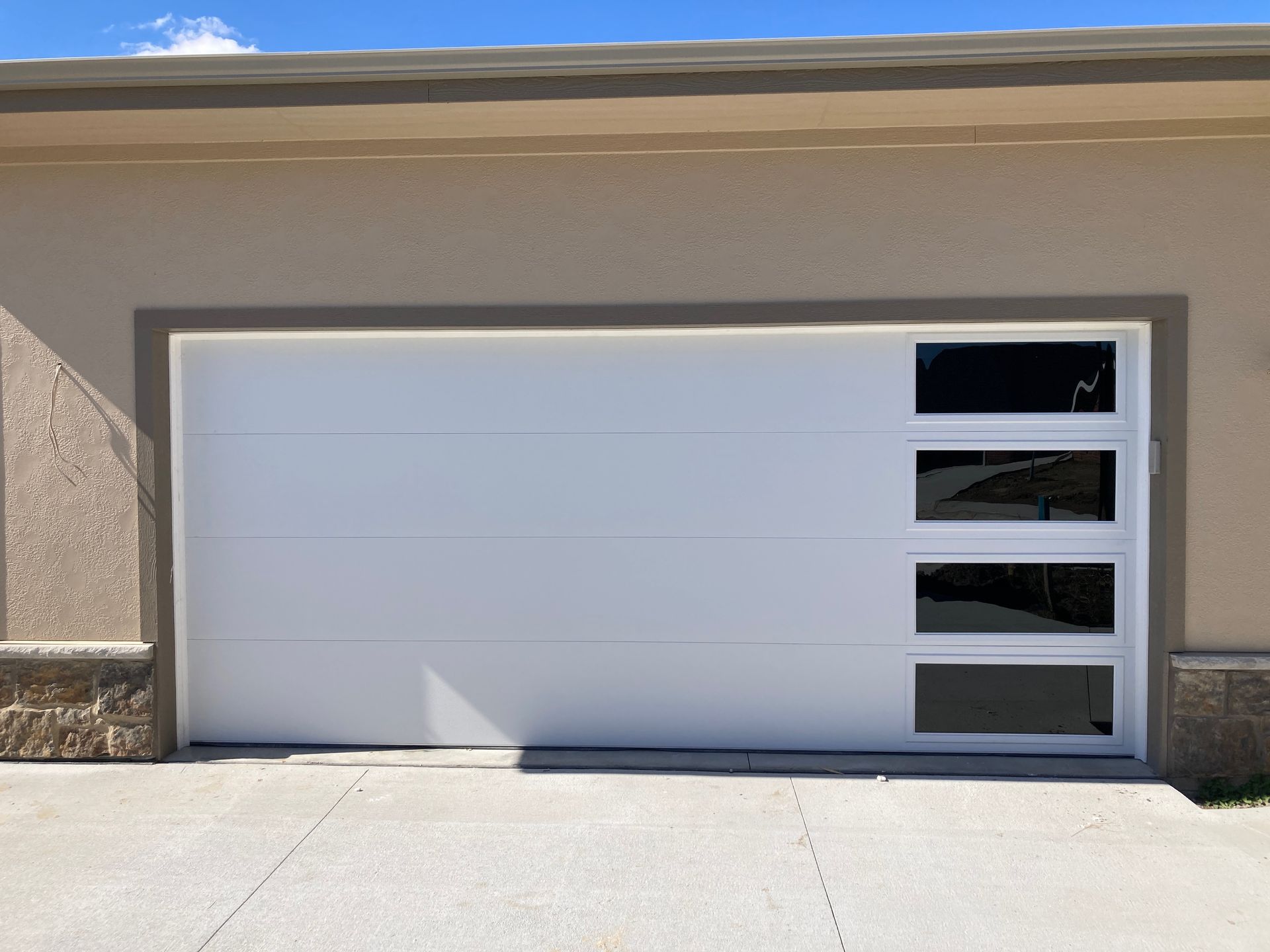 Modern white garage door with small windows on the right side, set in a stucco exterior wall.