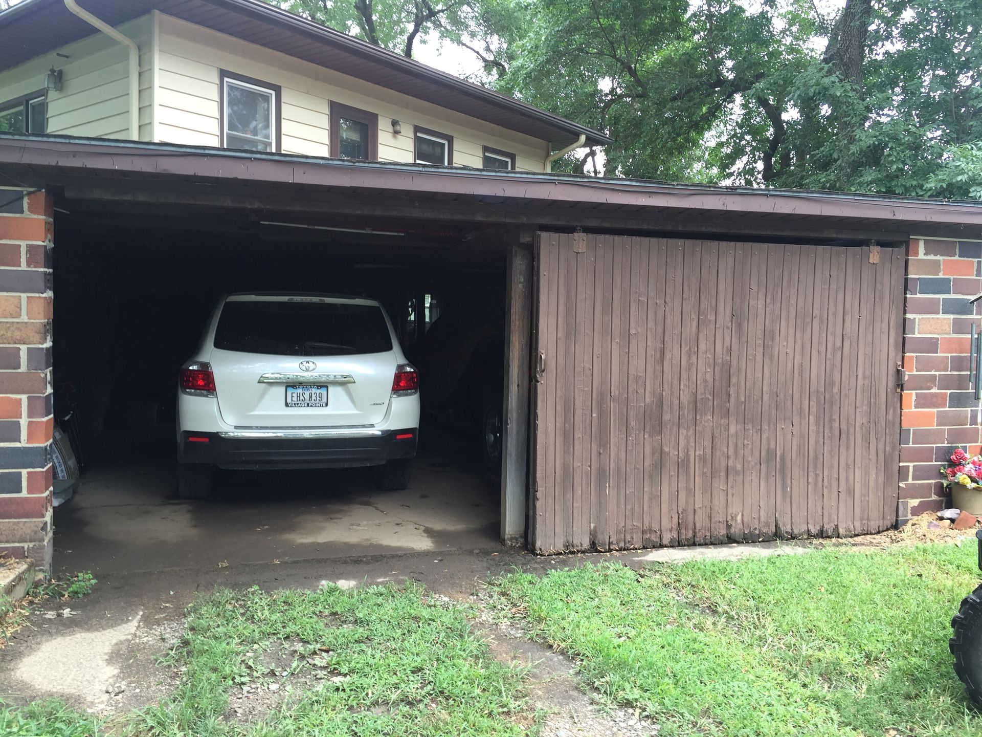 White SUV parked in a dark brick garage with a partially open wooden door