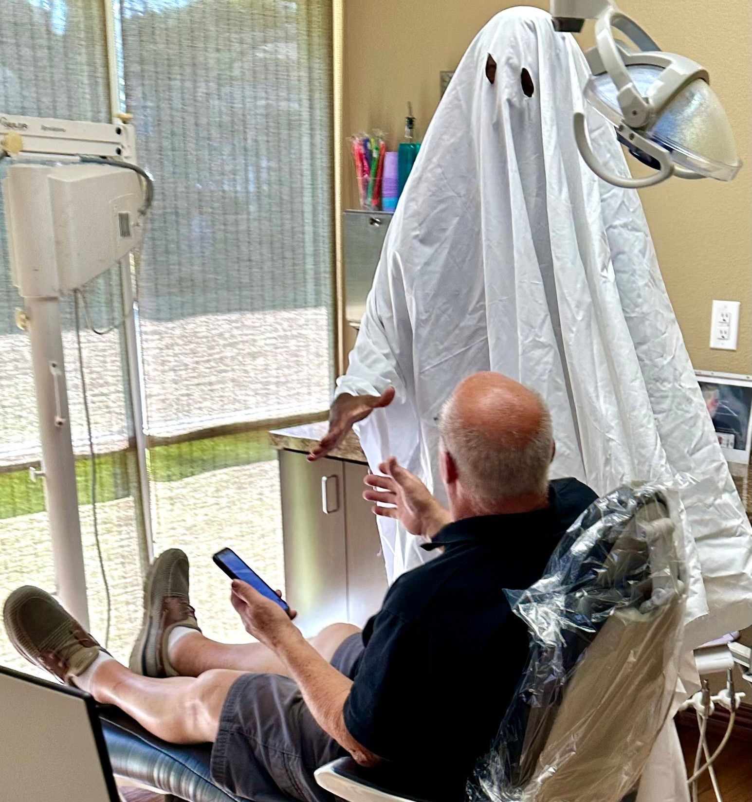A man is sitting in a dental chair with a ghost covering his head.