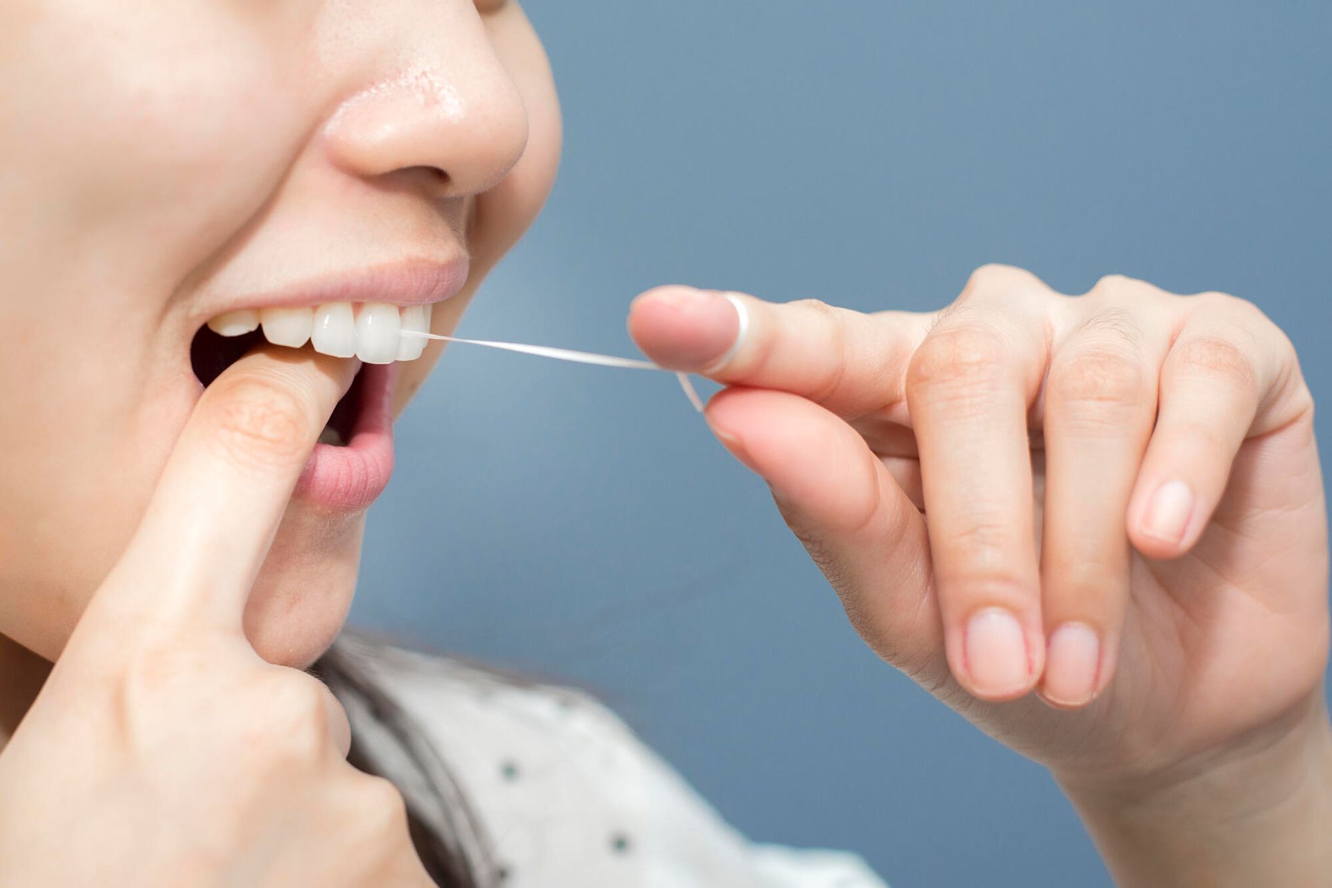 A woman is flossing her teeth with a dental floss.