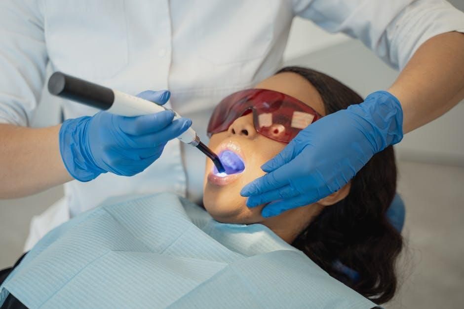 A woman is getting her teeth whitened by a dentist.