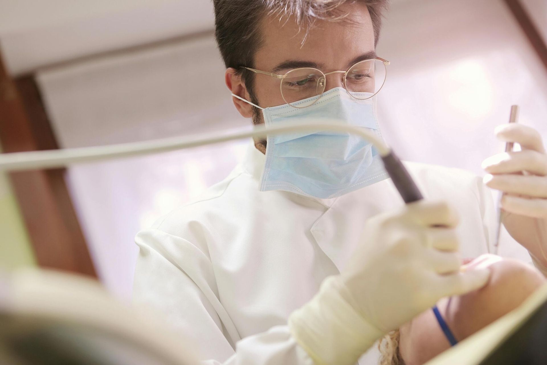 A dentist wearing a mask and gloves is working on a patient 's teeth.