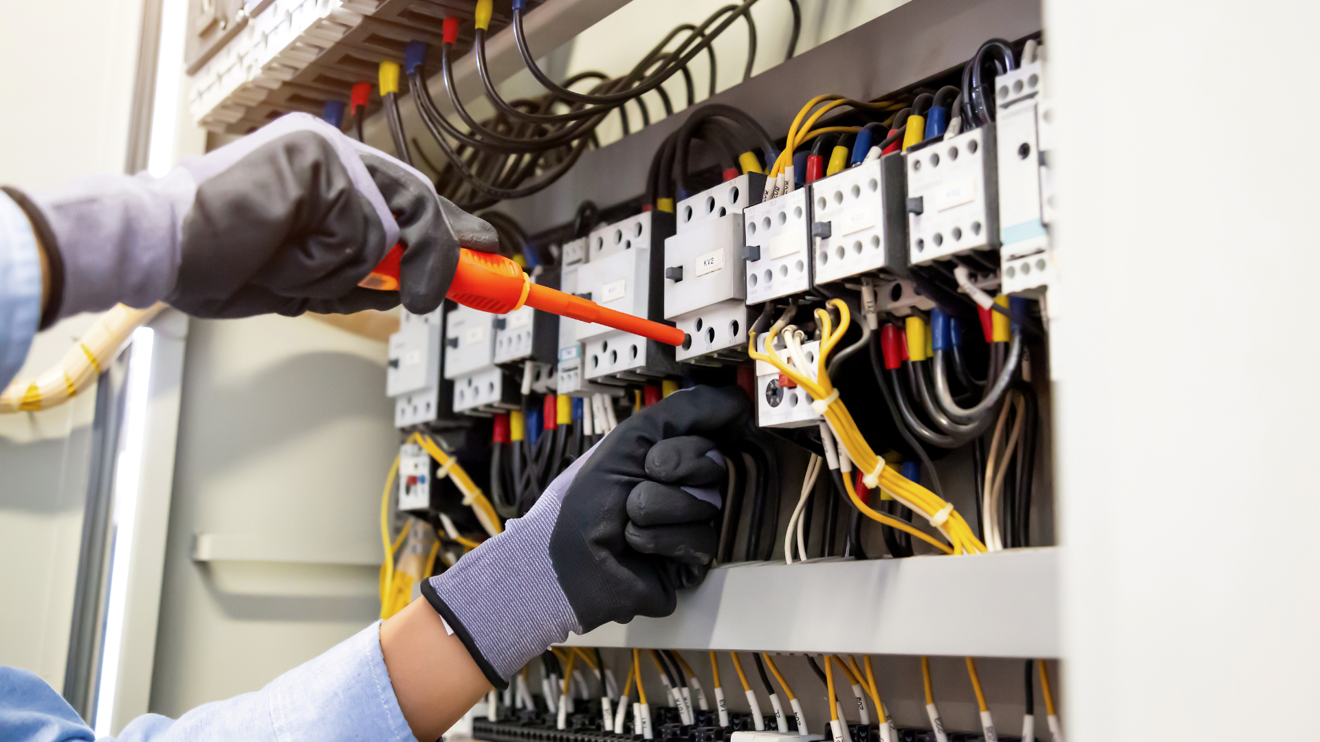 An electrician is working on an electrical box with a screwdriver.