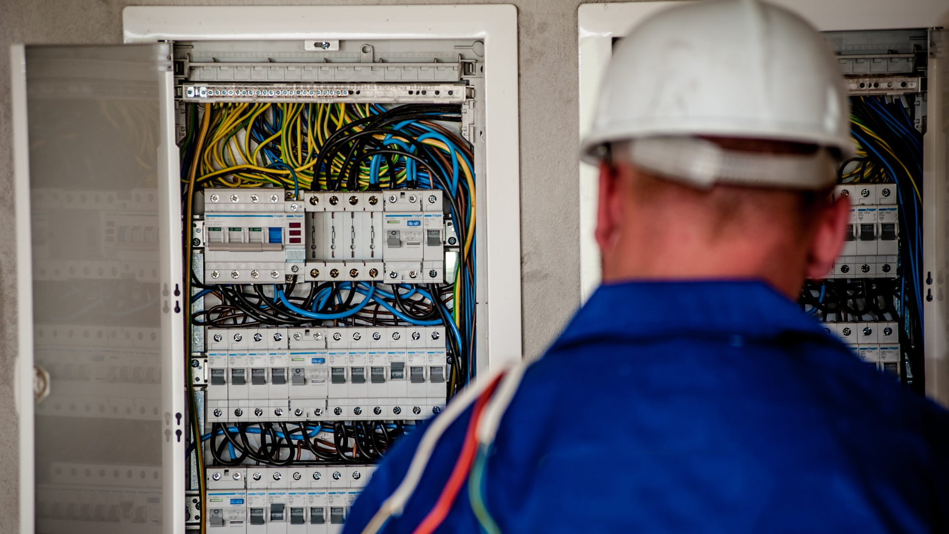 A man wearing a hard hat is looking at an electrical box.