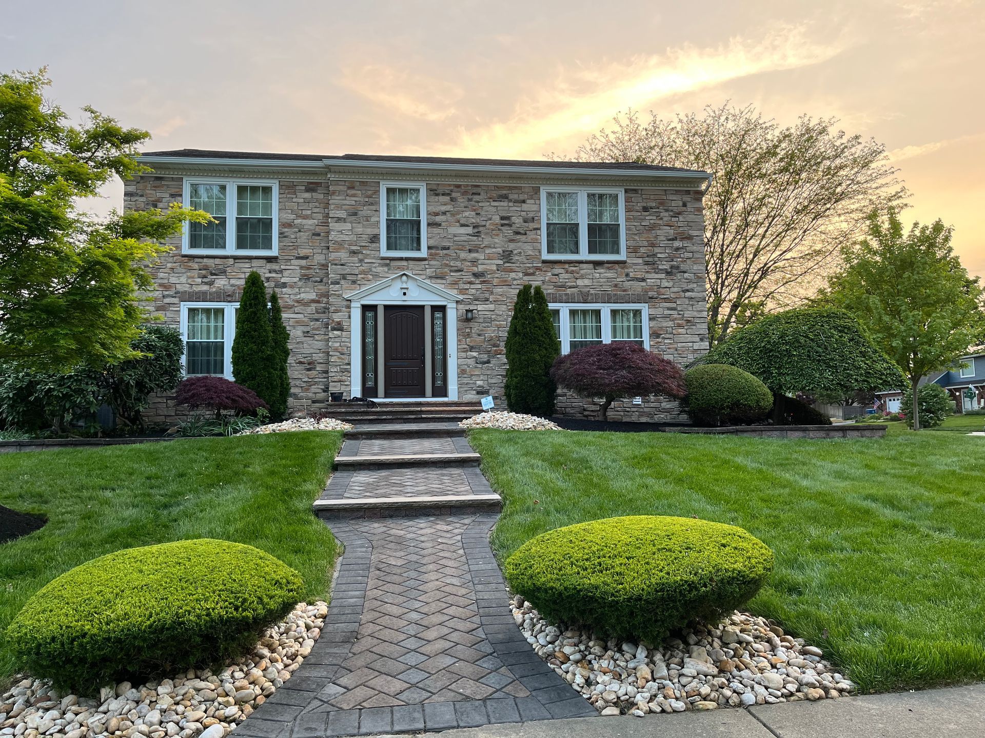 A large stone house with a lush green lawn and a brick walkway leading to the front door.