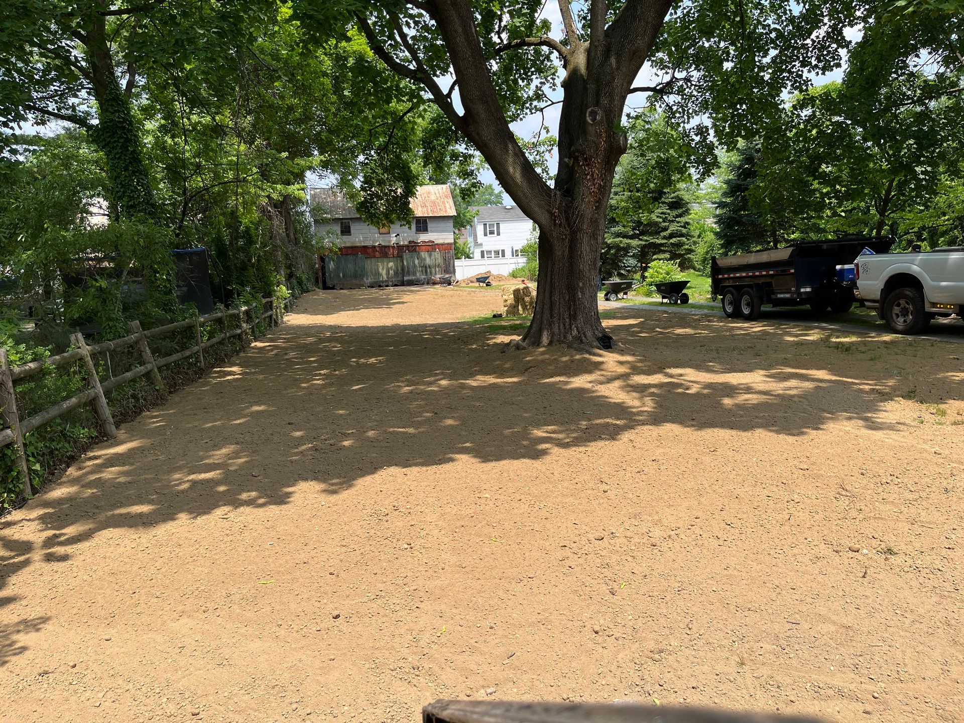 A truck is parked in a dirt lot next to a tree.