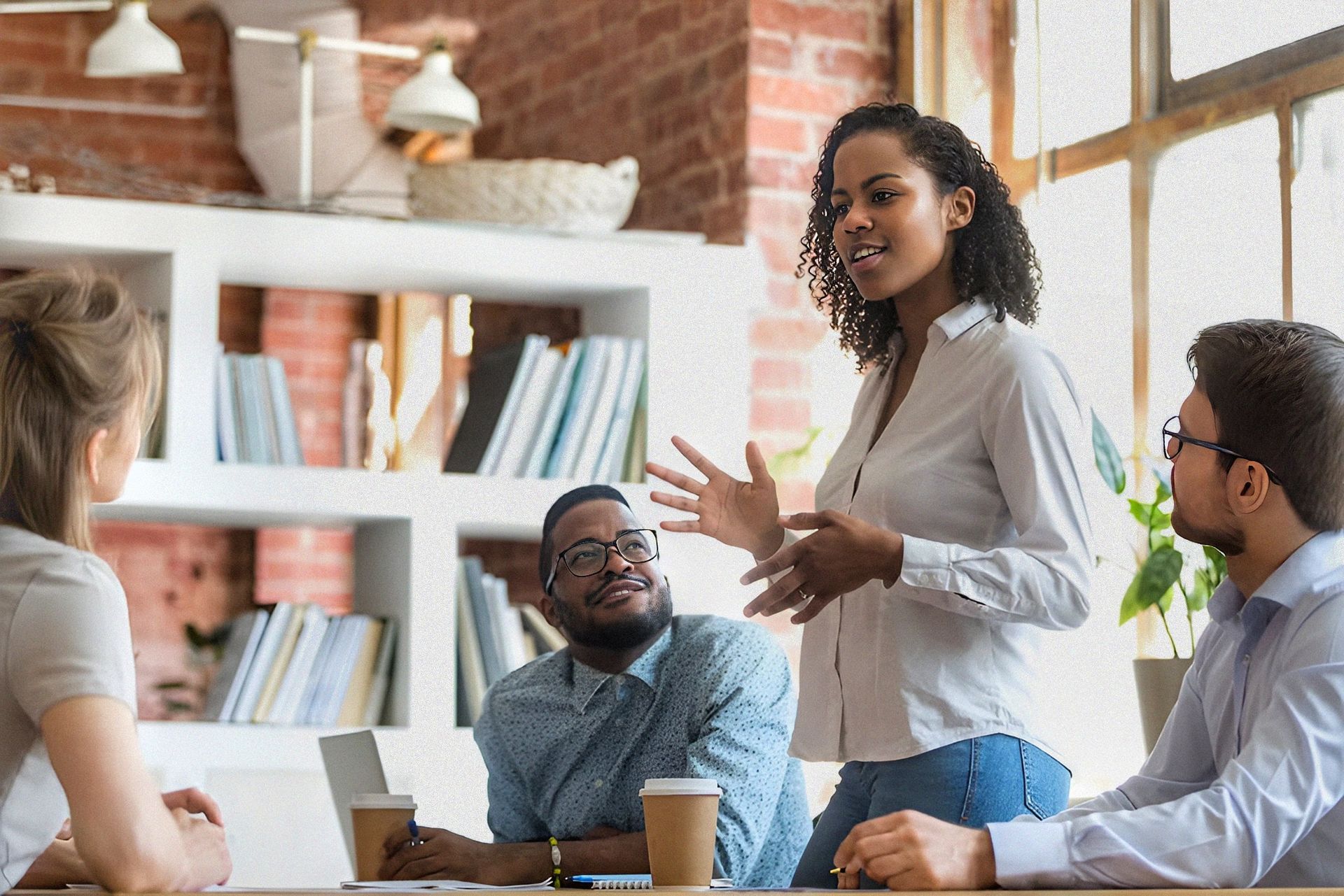 A woman is giving a presentation to a group of people sitting around a table.