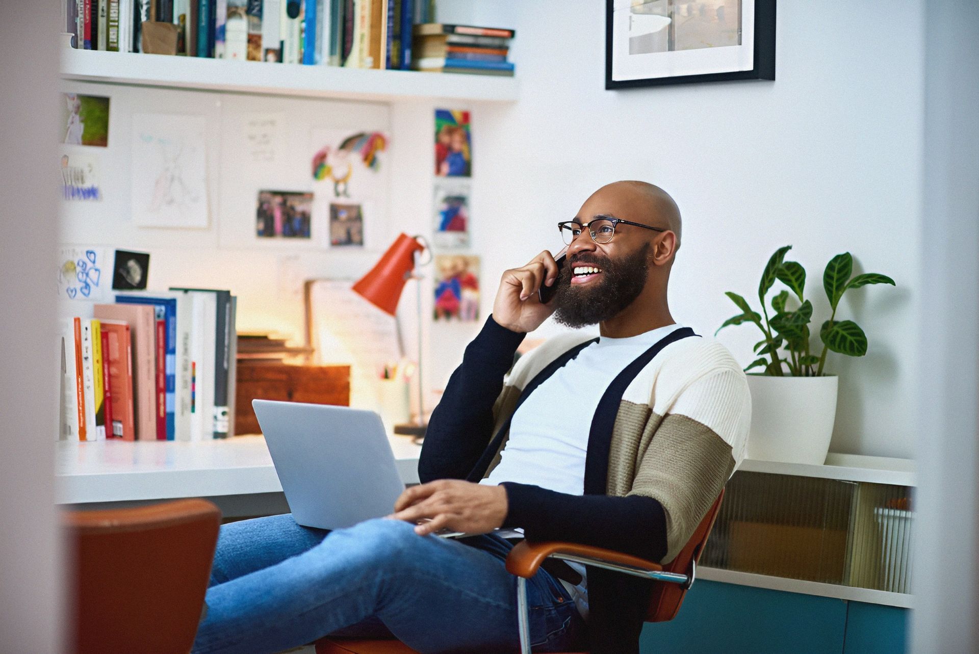 A man is sitting in a chair with a laptop and talking on a cell phone.