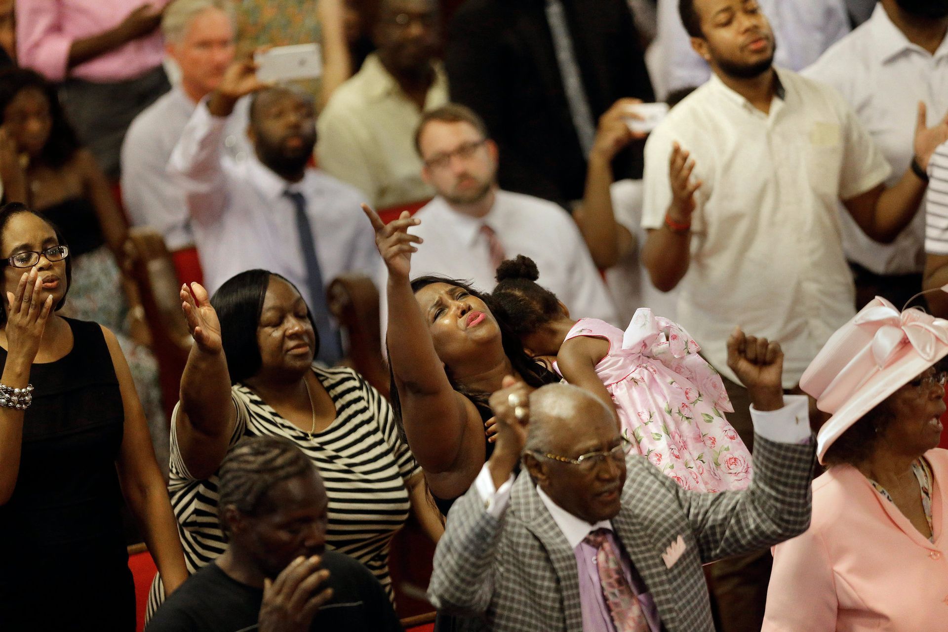 A crowd of people are sitting in a church with their hands in the air.