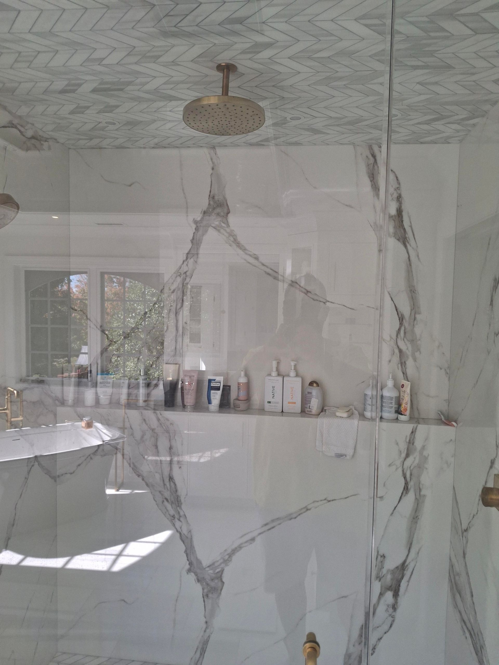 A bathroom with marble walls , a bathtub , and a shower head.
