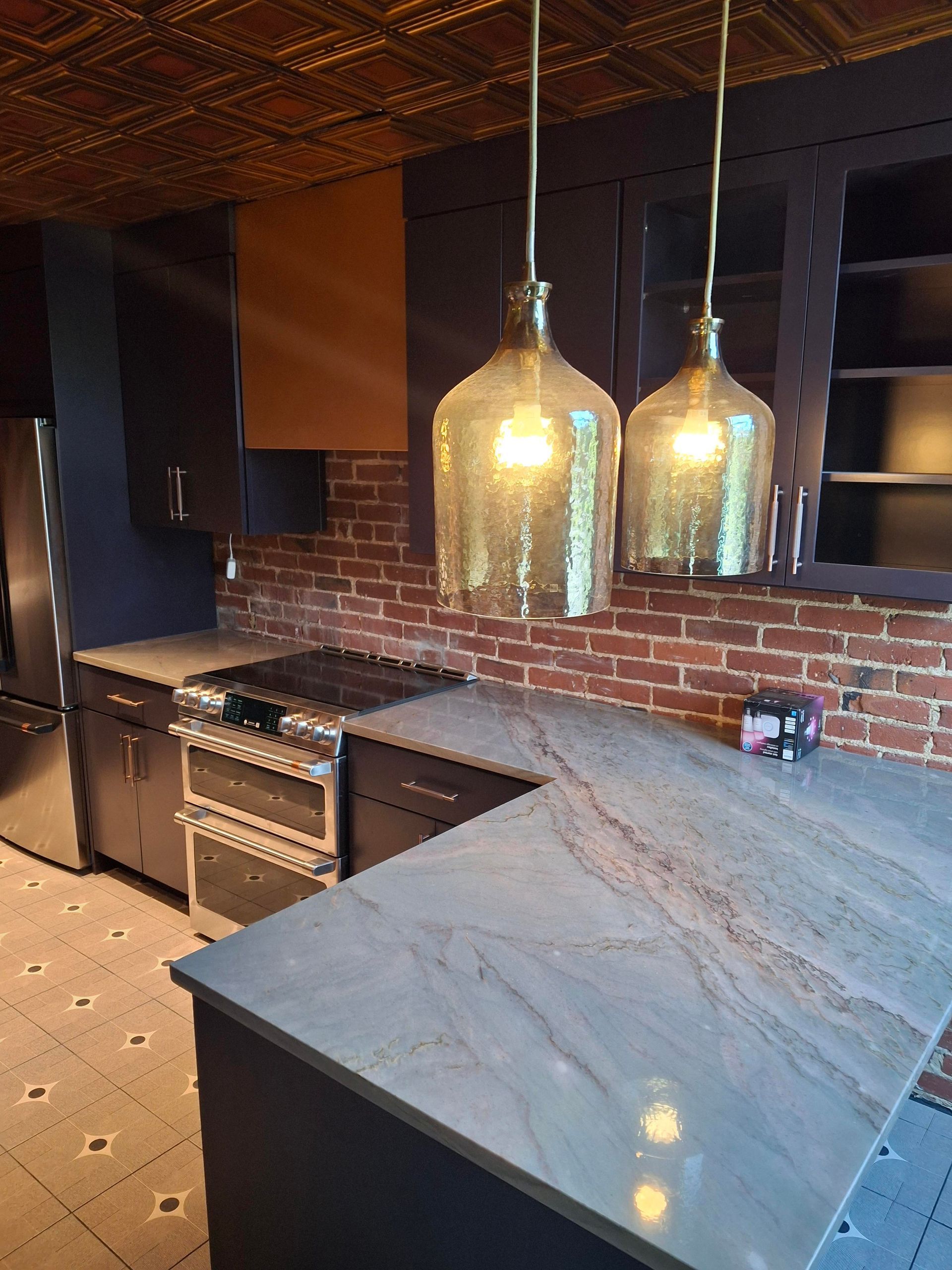 A kitchen with a brick wall , stainless steel appliances , granite counter tops , and pendant lights.