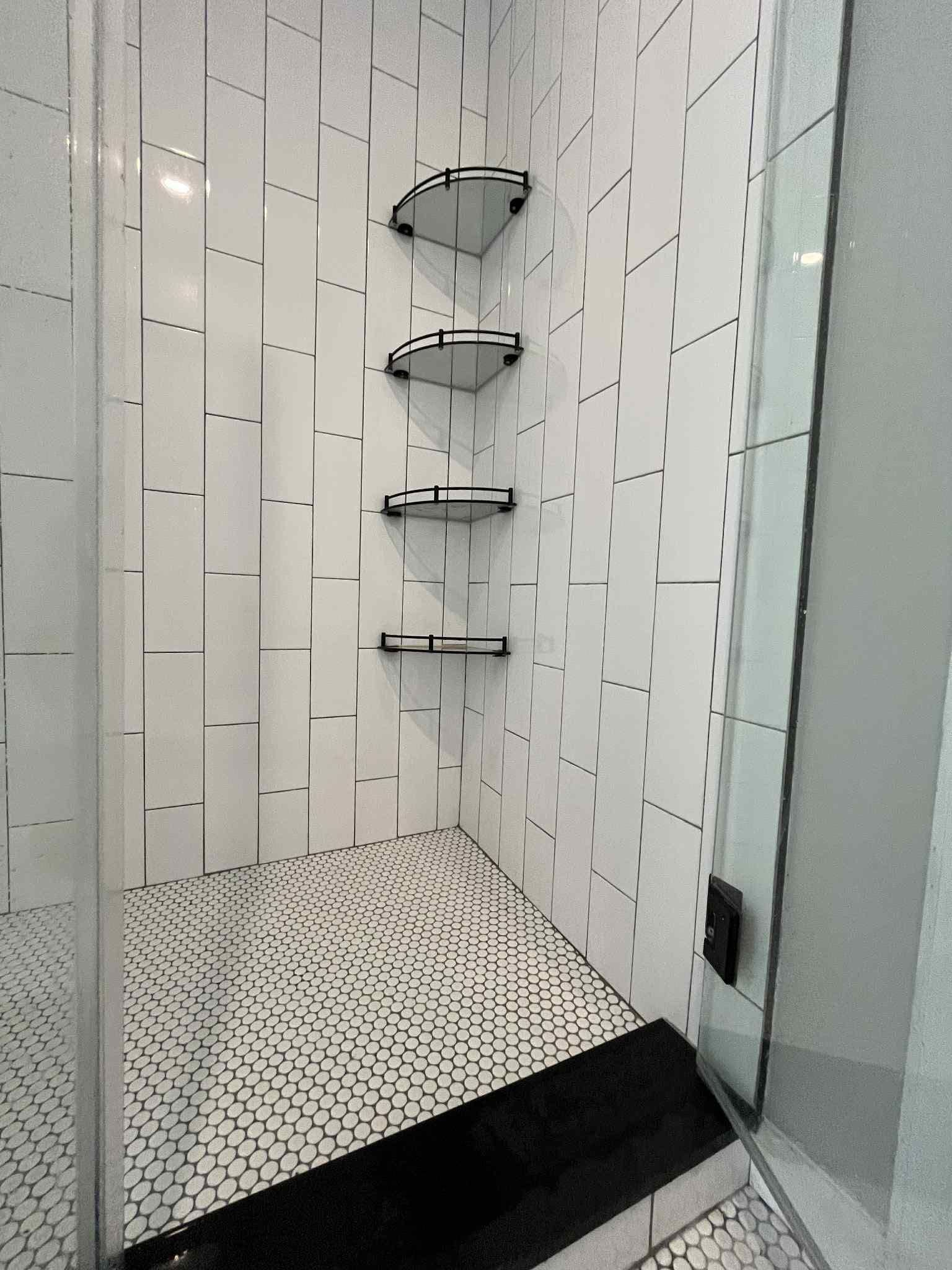 A shower with a black and white tile floor and corner shelves.