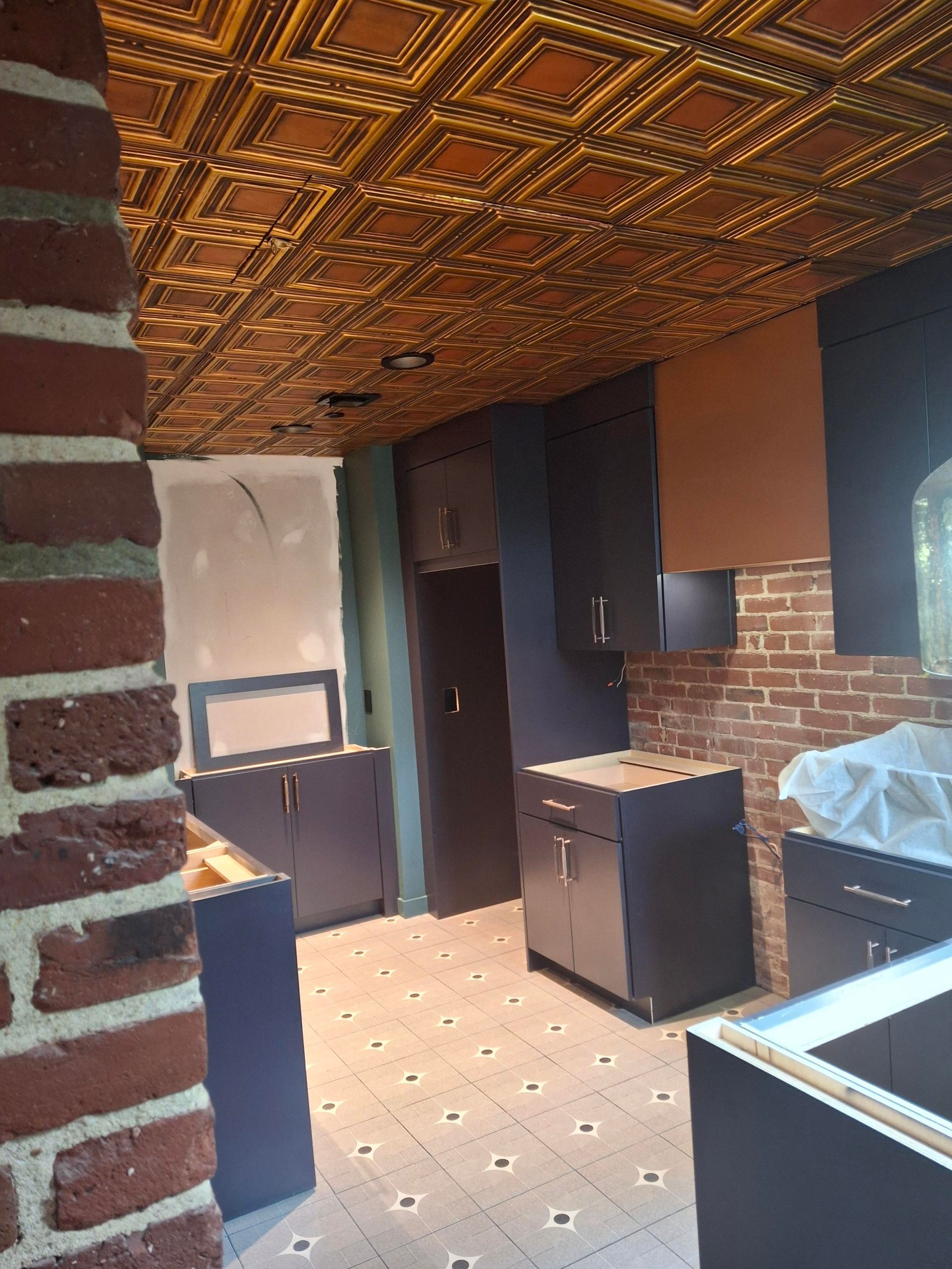 A kitchen with a tiled ceiling and a brick wall