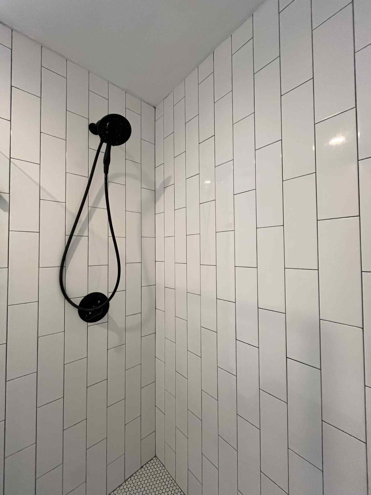 A shower with white tiles and a black shower head.