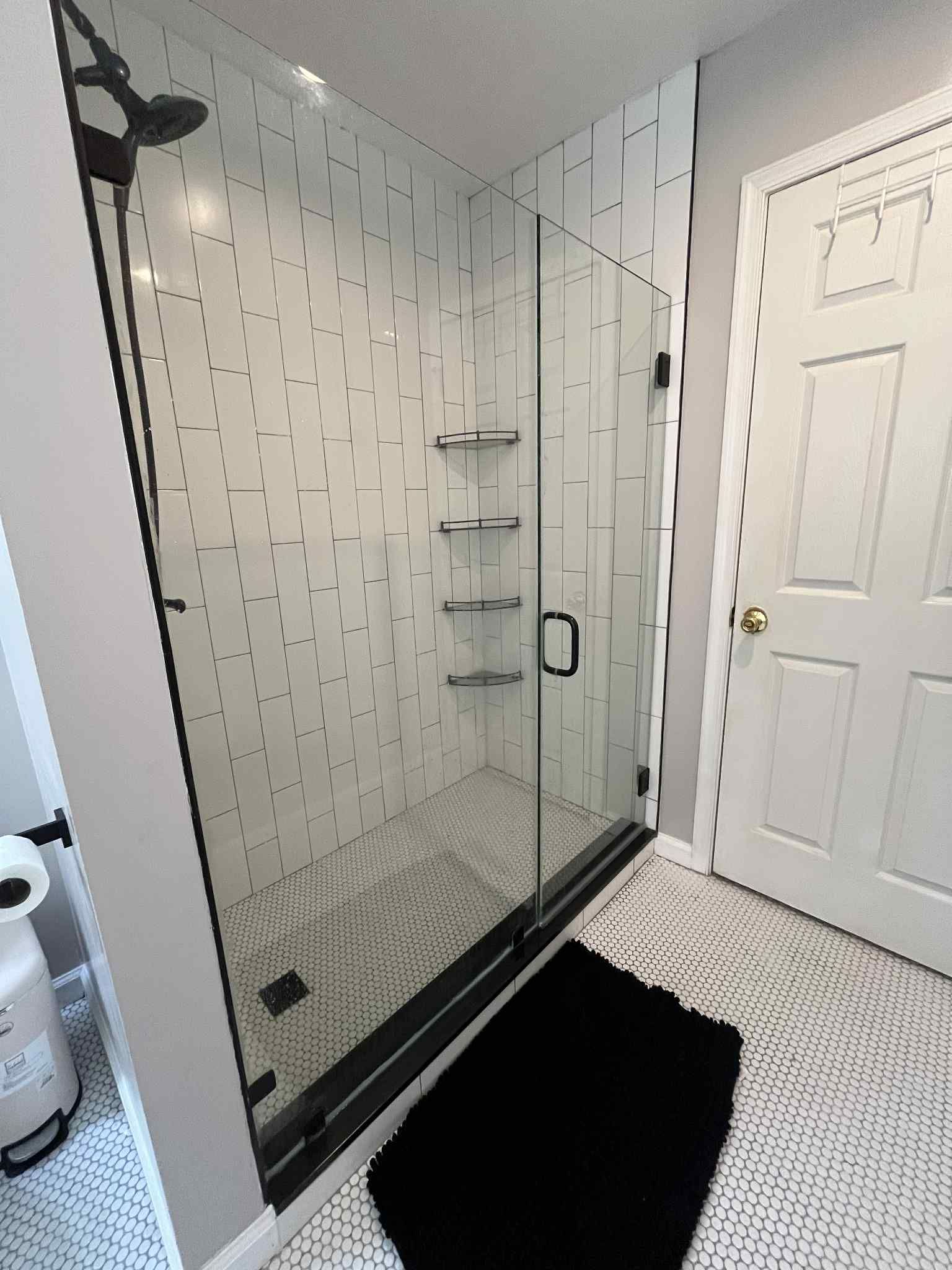 A bathroom with a walk in shower and a black rug.