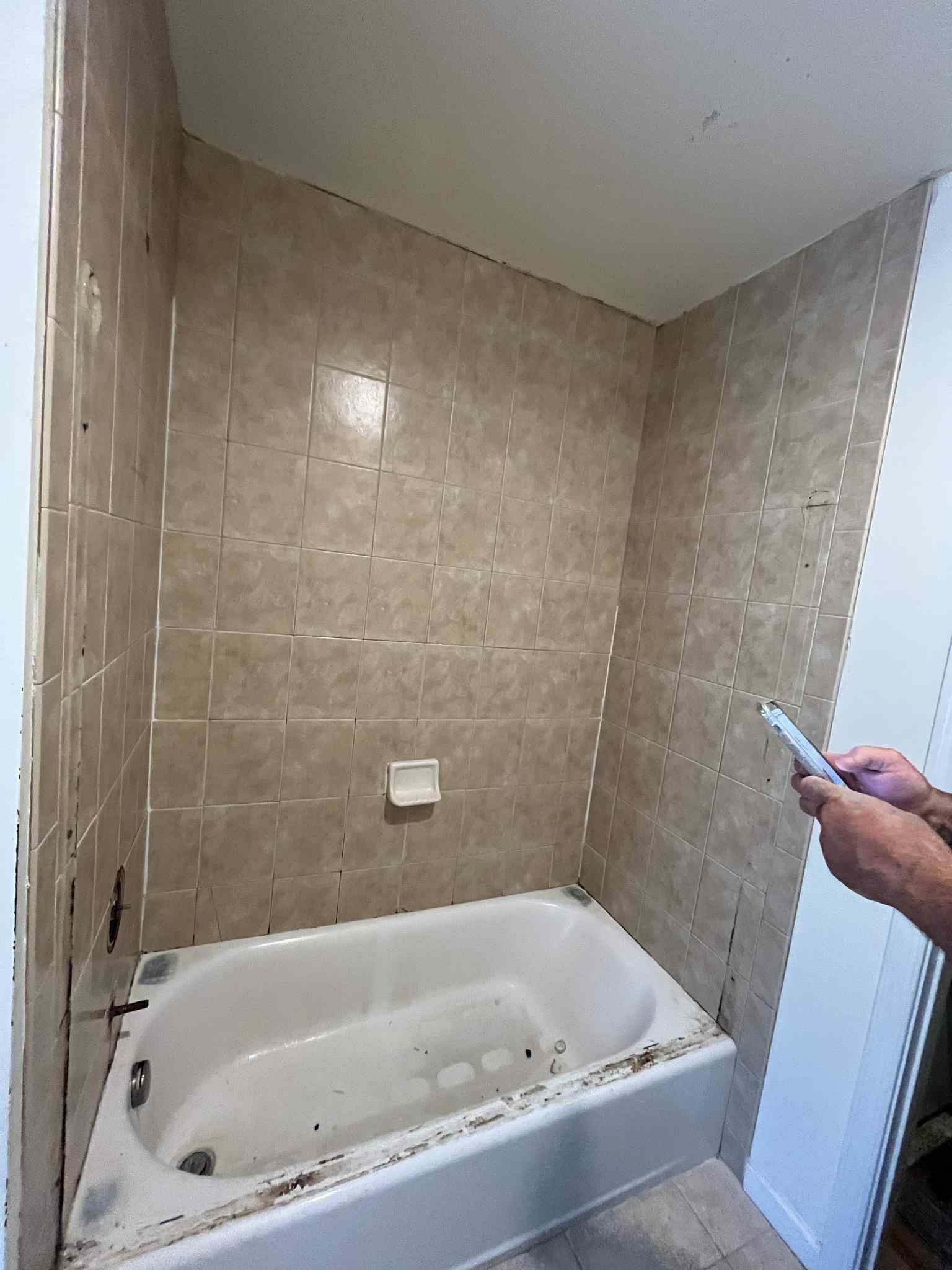 A person is standing next to a bathtub in a bathroom.