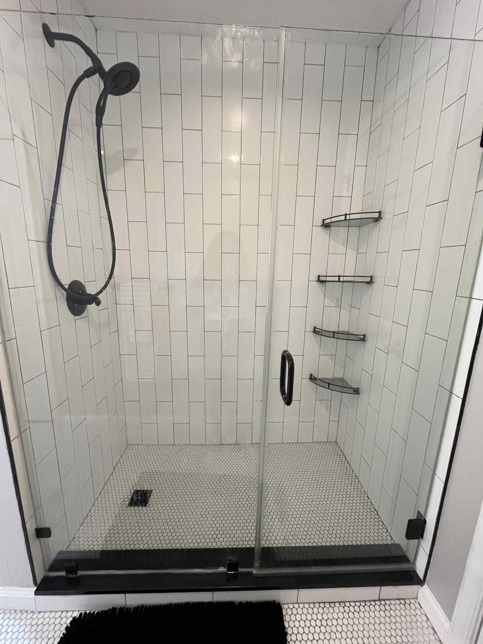 A shower stall with a black shower head and a black mat.