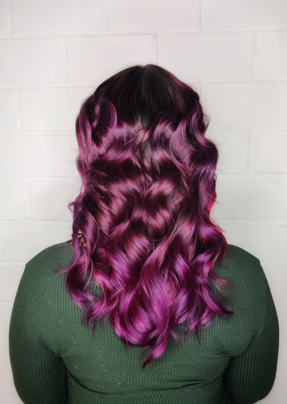Woman with wavy hair; dark roots fade to vibrant purple and pink.