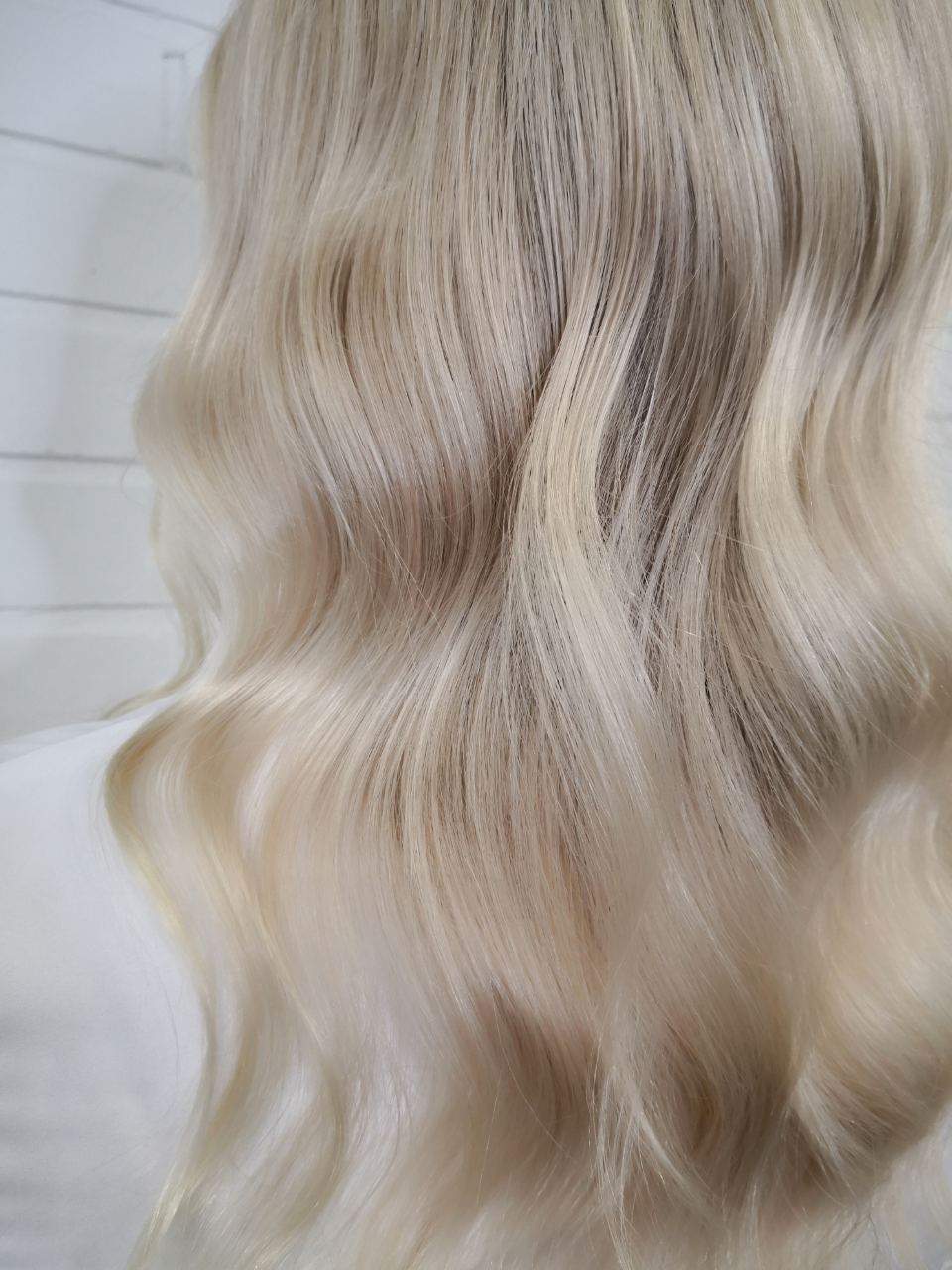 Blonde hair styled in loose waves, with darker roots showing, against a white background.