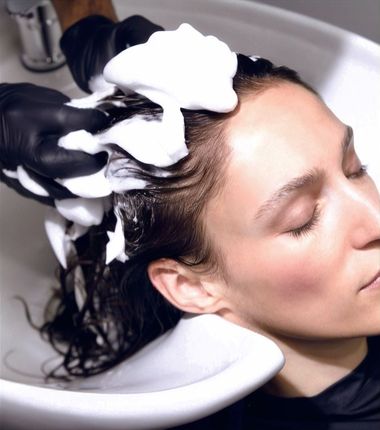 Person getting hair washed in a salon basin with foam. Hands in black gloves.