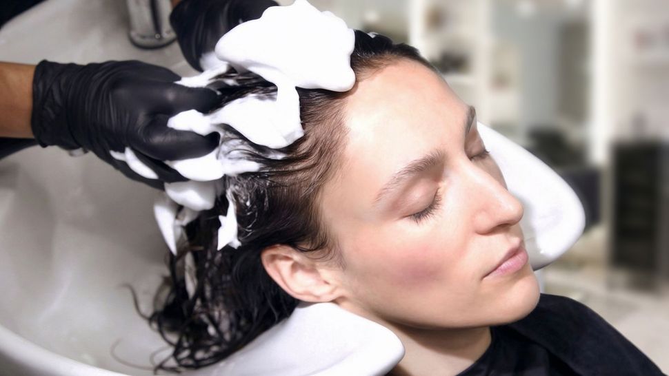 Person getting hair washed in a salon, eyes closed, hands with black gloves in hair.