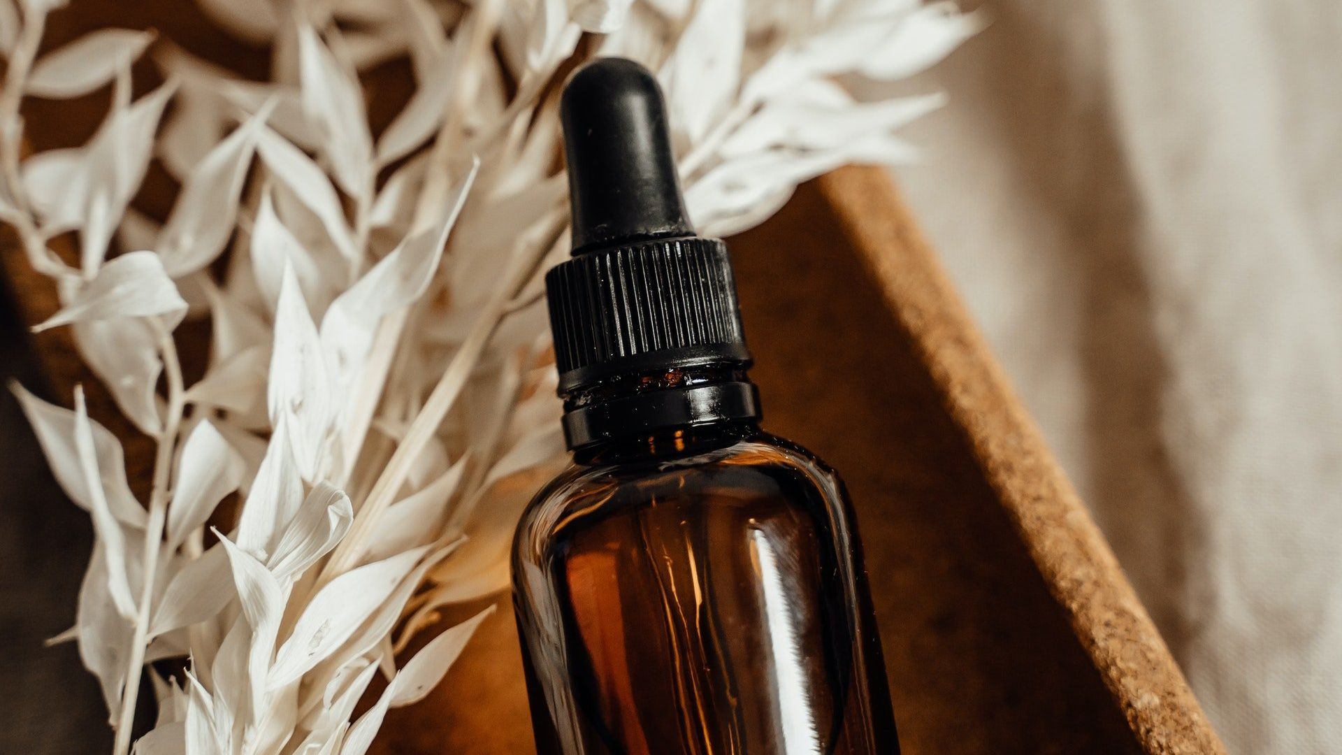 A bottle of essential oil with a dropper on top of a wooden bowl.