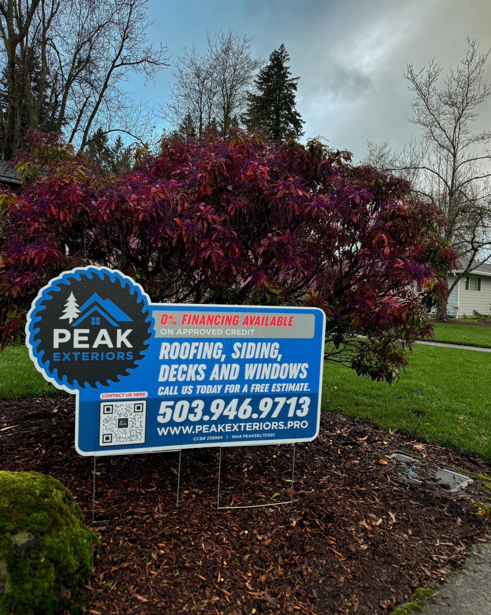 A yard sign for Peak Exteriors advertising roofing, siding, decks, and windows with a phone number and website.