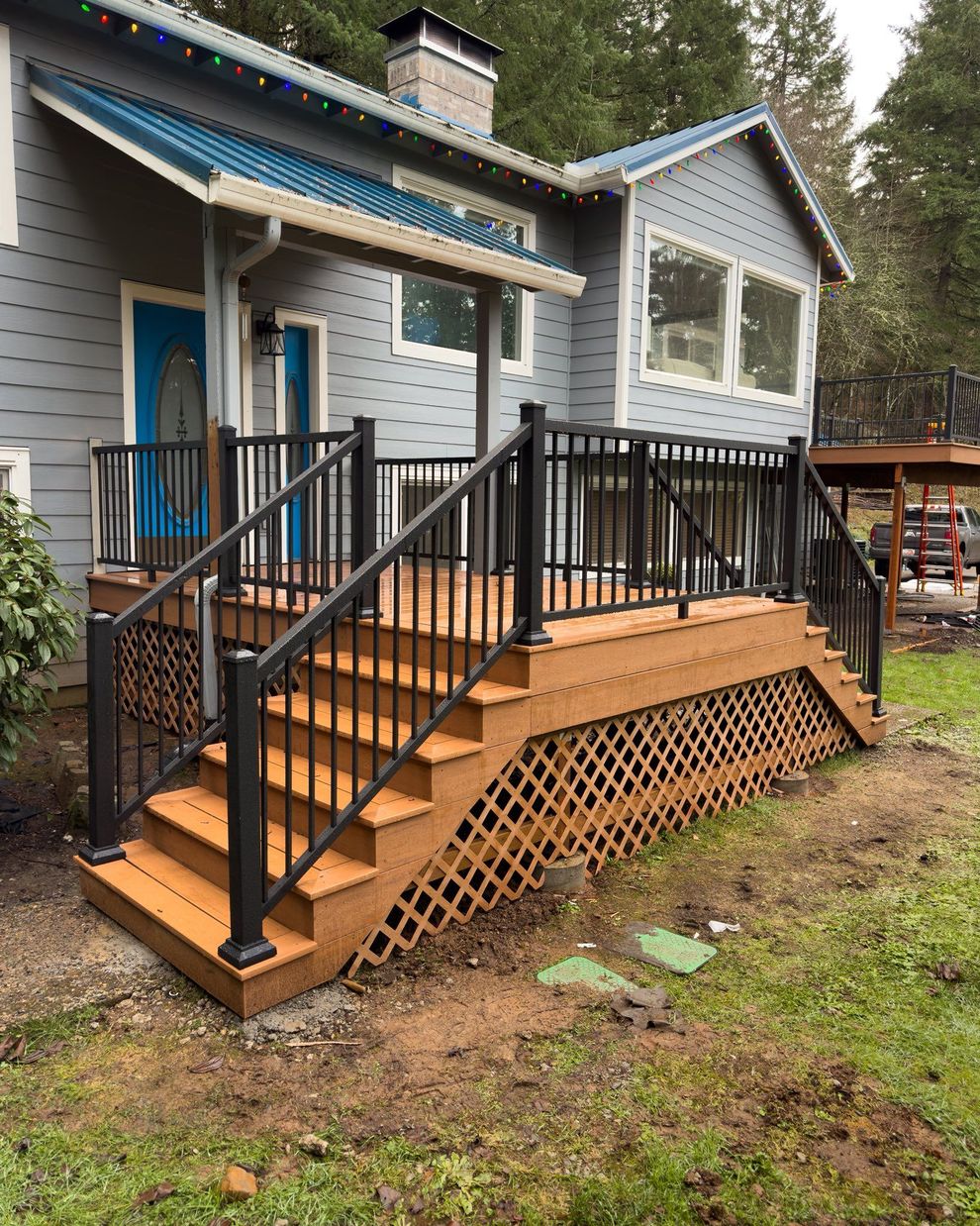 A house exterior featuring a newly built brown wooden deck and stairs with black railings, set against a grey-sided home.