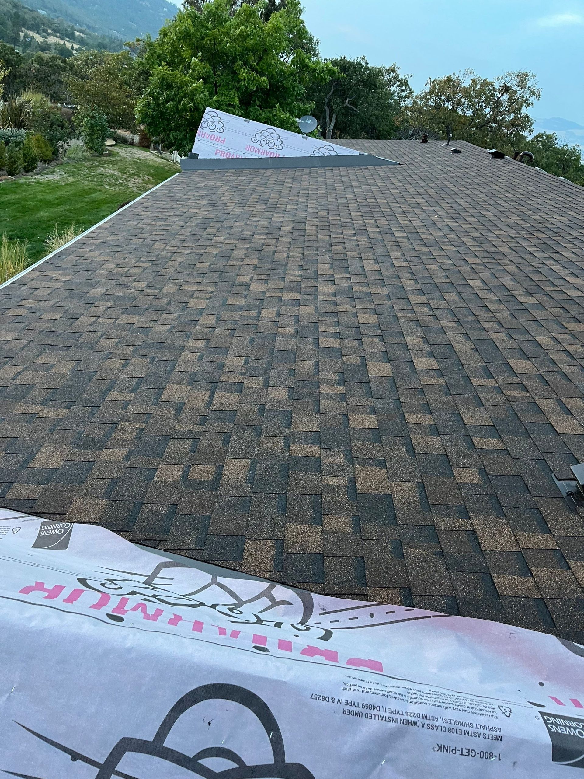 A partially shingled roof with exposed underlayment in the foreground and a triangular section of white material above.