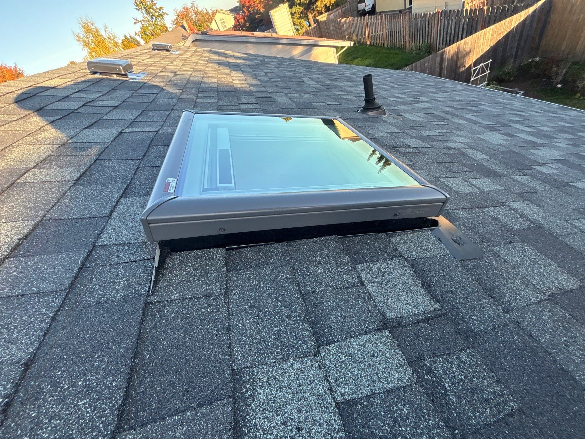 A modern rectangular skylight installed on a grey asphalt shingle roof during the day.