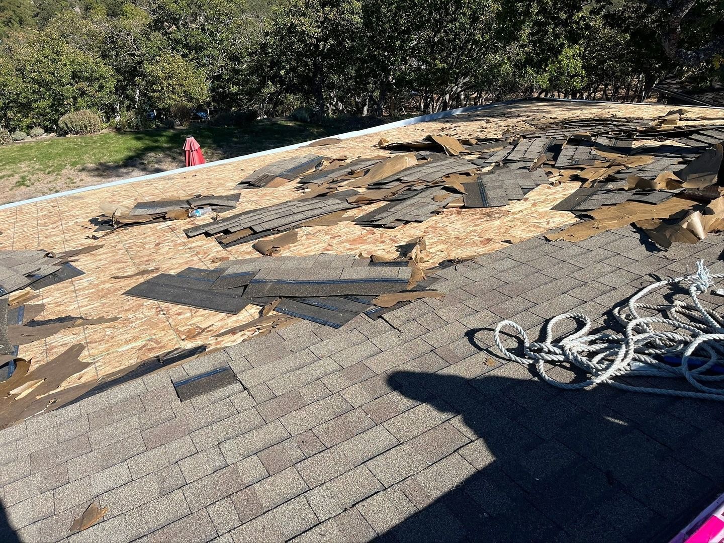 A roof renovation in progress with removed shingles scattered on exposed plywood decking under a sunny sky.