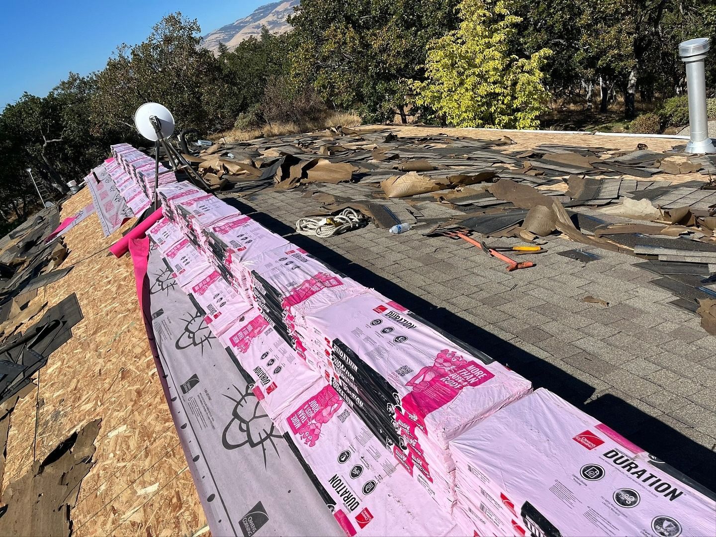 A roof undergoing repairs with stacks of pink Owens Corning Duration shingles placed along the ridge.