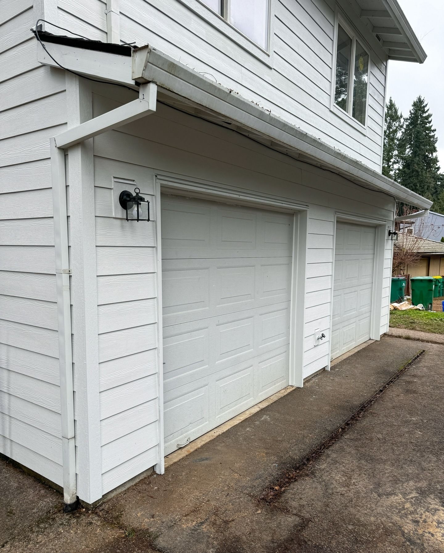 A two-car garage with white horizontal siding and two white garage doors, viewed from a gravel driveway.