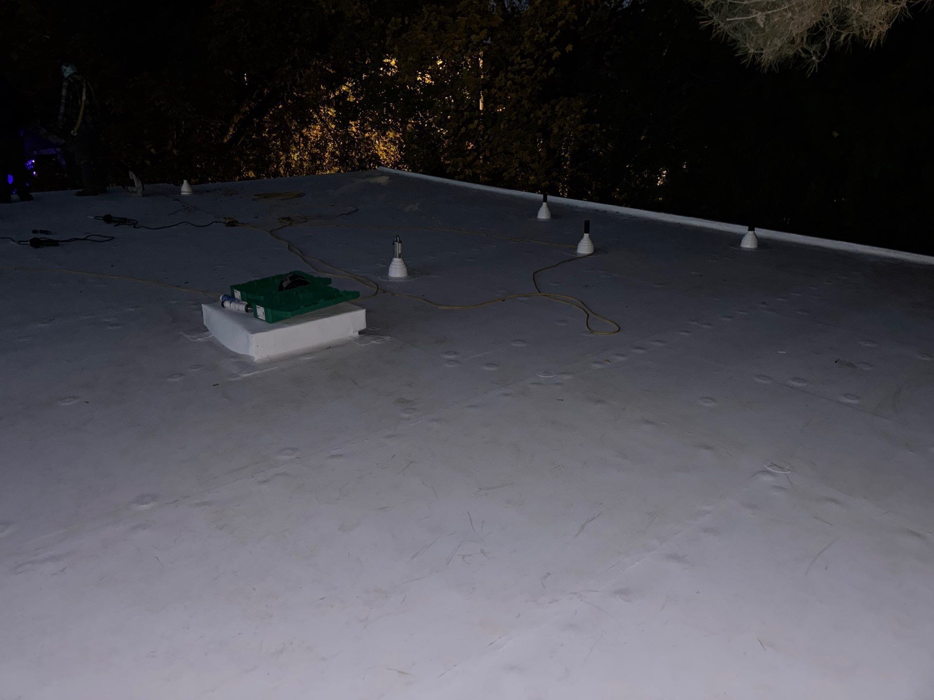 A low-angle night view of a flat white roof with a green equipment box and several small, evenly spaced light fixtures.