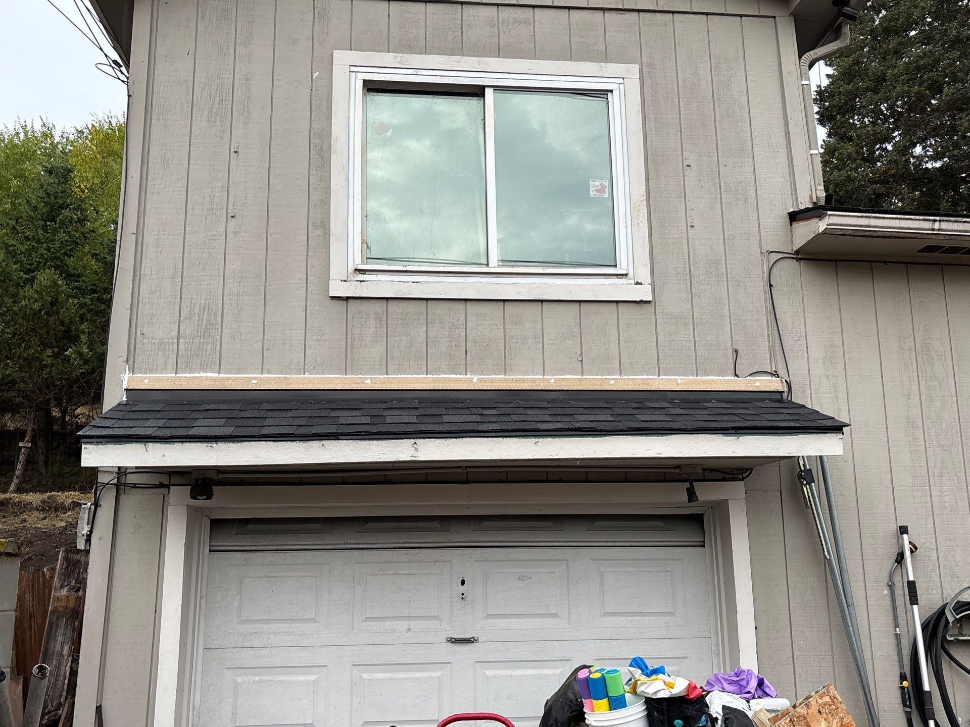 A two-story building exterior with a white garage door, a new black shingled awning, and an upper-level window.