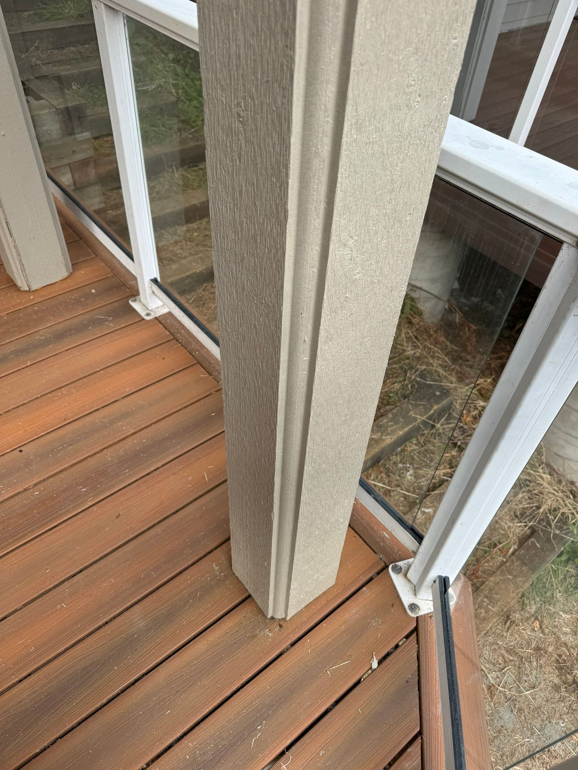 A close-up view of a textured, light-gray porch support post, framed by white metal railing and a wood-slatted deck.