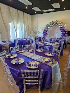 A room filled with tables and chairs decorated in purple and silver for a party.