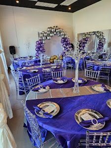 A room filled with tables and chairs decorated in purple and silver for a wedding reception.