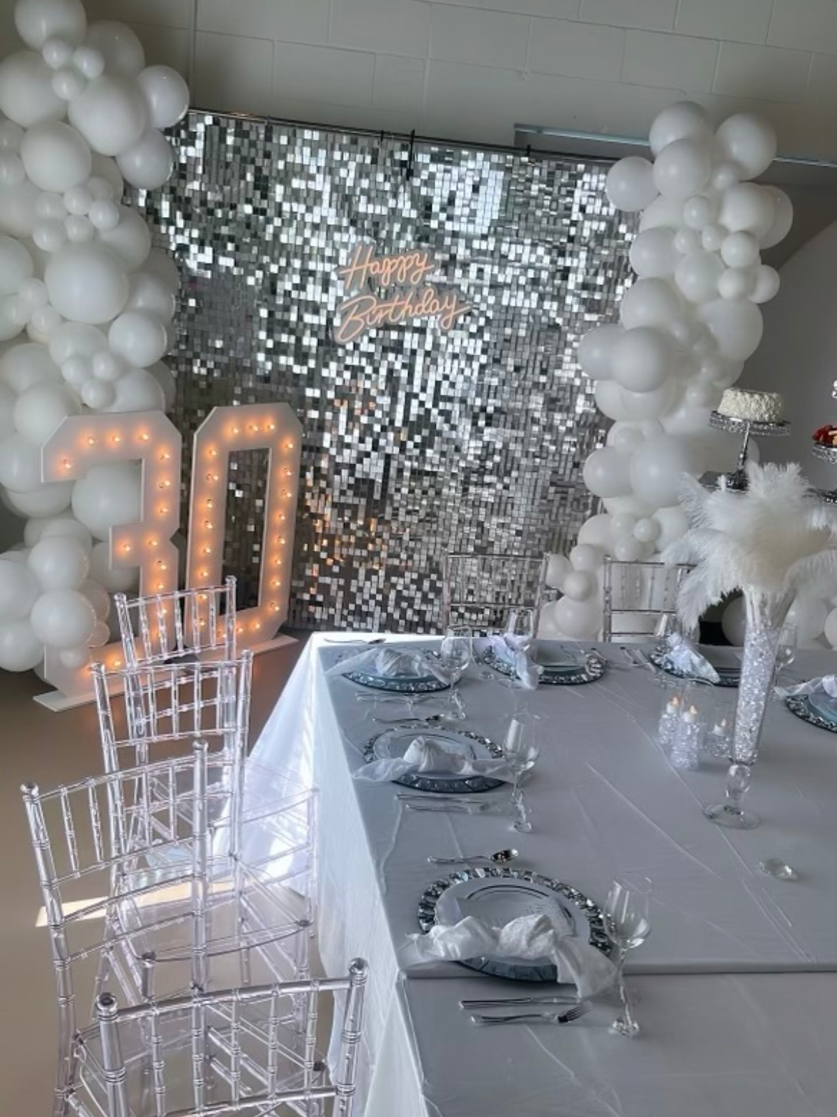A long table with plates , glasses , and balloons on it.